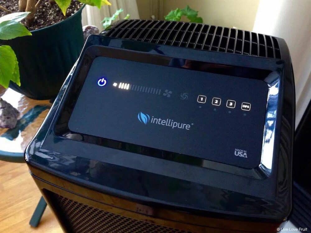 The control panel on a black Intellipure air purifier shows the blue power button, a medium fan speed, and an official Intellipure logo.