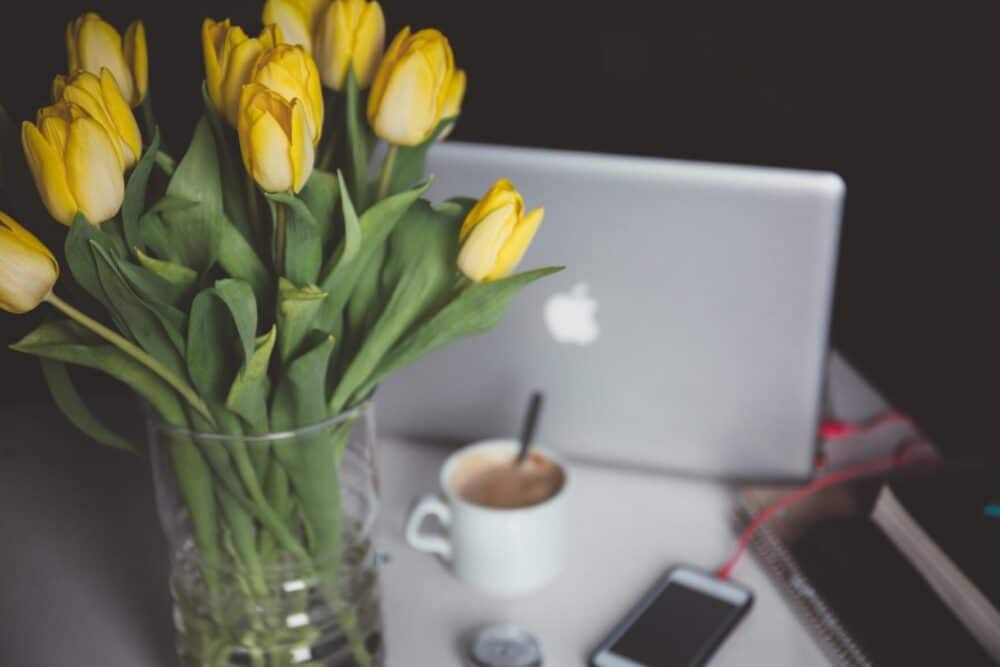 yellow flowers on a desk with a computer and coffee