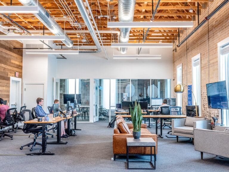 The inside of an office space with people sitting at tables working on computers. There is a communal seating area in the front of the room.